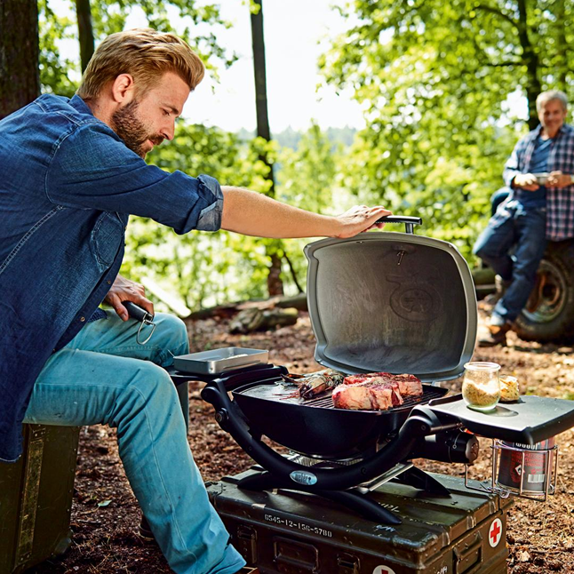 camping man opening portable grill with meat cooking